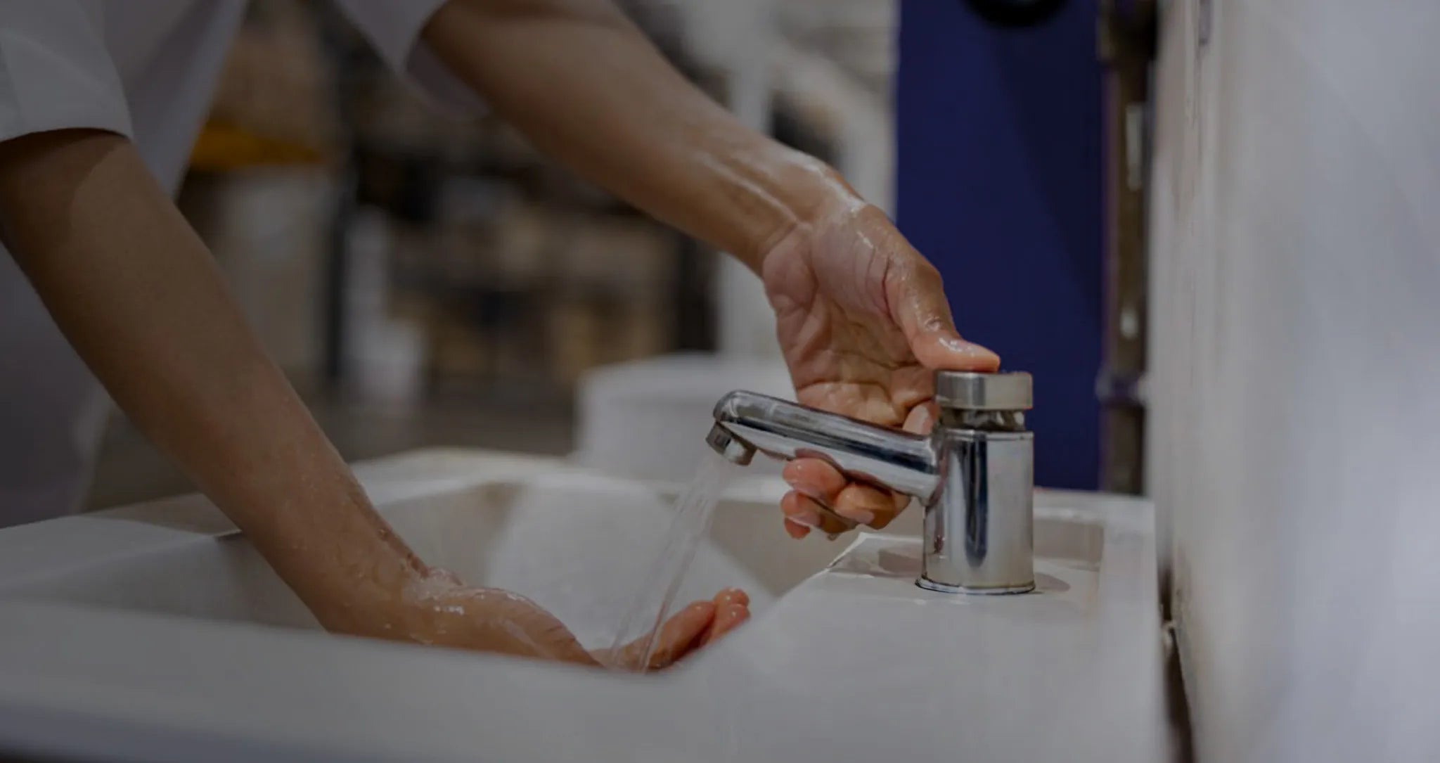 Person washing hands under running water at a commercial sink, emphasizing the importance of hygiene and contamination control in healthcare environments.