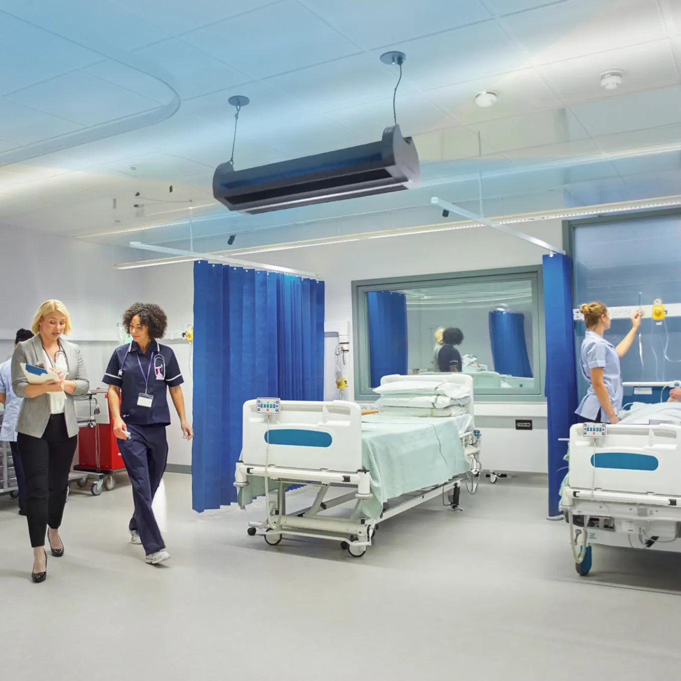 Hospital room with healthcare workers and ceiling-mounted UV disinfection unit, demonstrating how upper-air GUV systems target airborne pathogens by neutralizing them in the upper atmosphere using safe UV-C light.