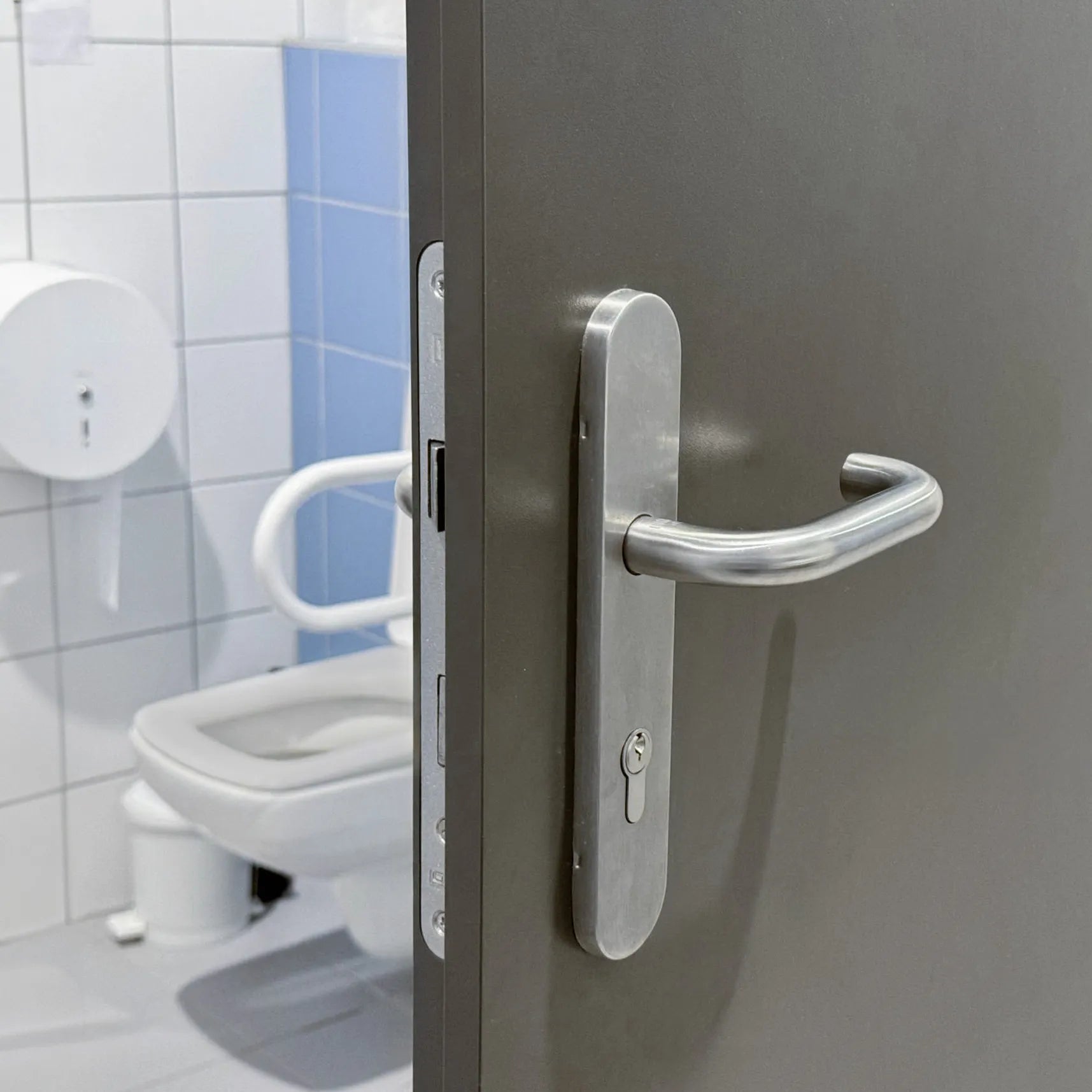 Close-up of a hospital door handle in a bathroom, illustrating Prescientx self-disinfecting surface technology for high-touch areas.
